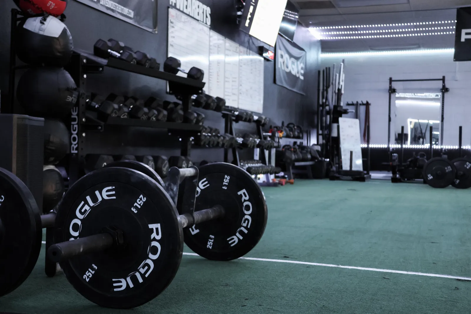 The RTS Fitness training floor with loaded barbells, dumbbells, slam balls and green turf.