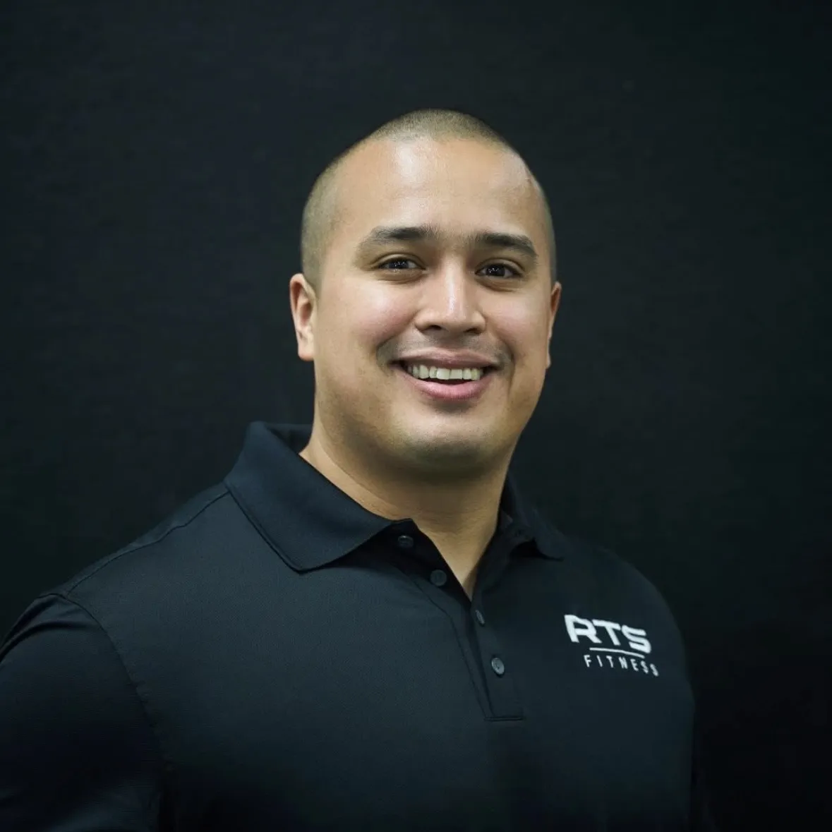 Coach Gonz of RTS Fitness, smiling in a black RTS polo against a dark wall.